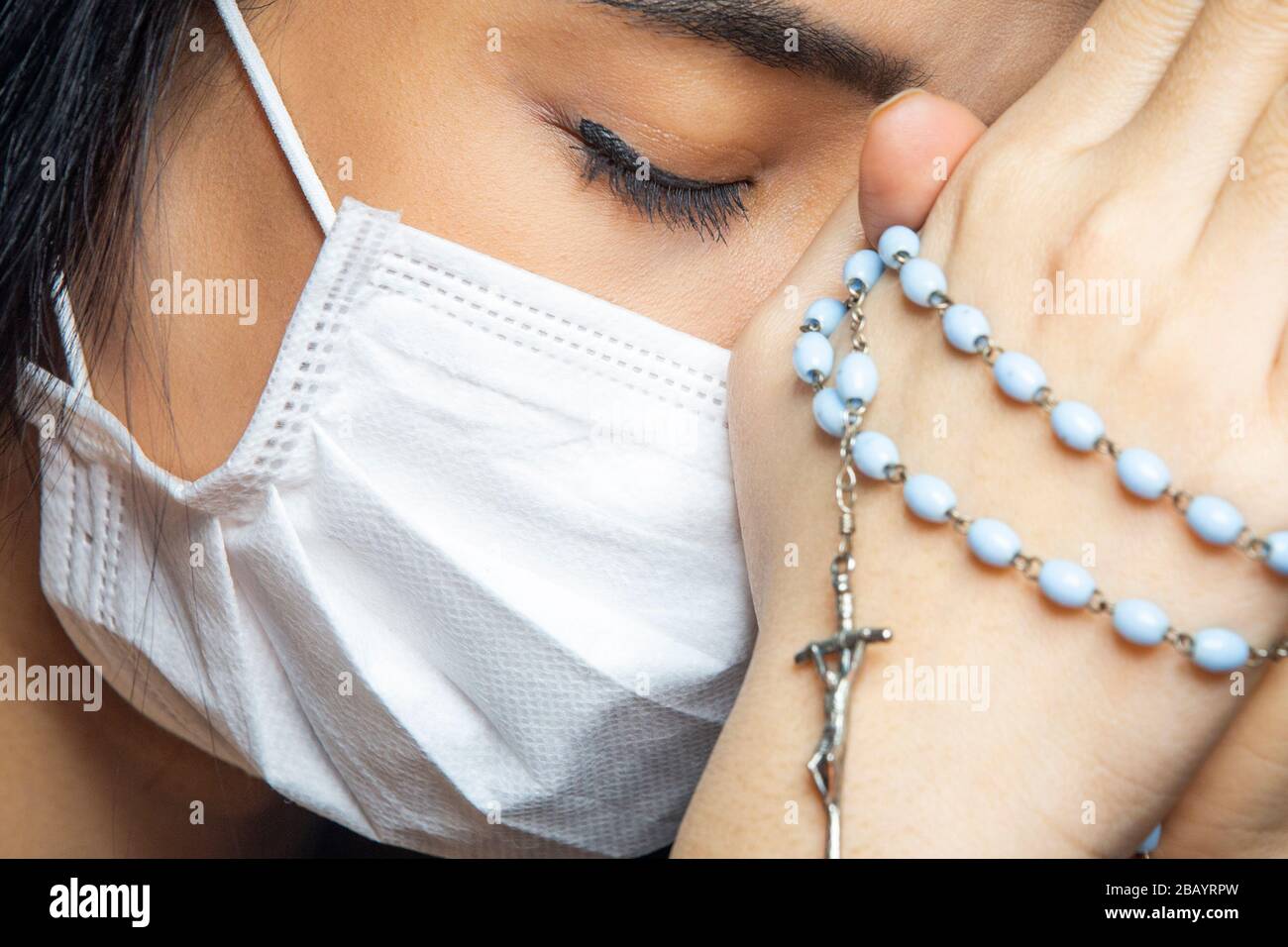 Femme portant un masque chirurgical priant avec un rosaire. La religion chrétienne espère concept. Banque D'Images