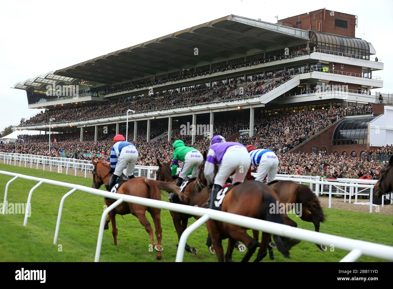 Les chevaux et les jockeys passent devant le grand stand aux courses de Cheltenham. Banque D'Images
