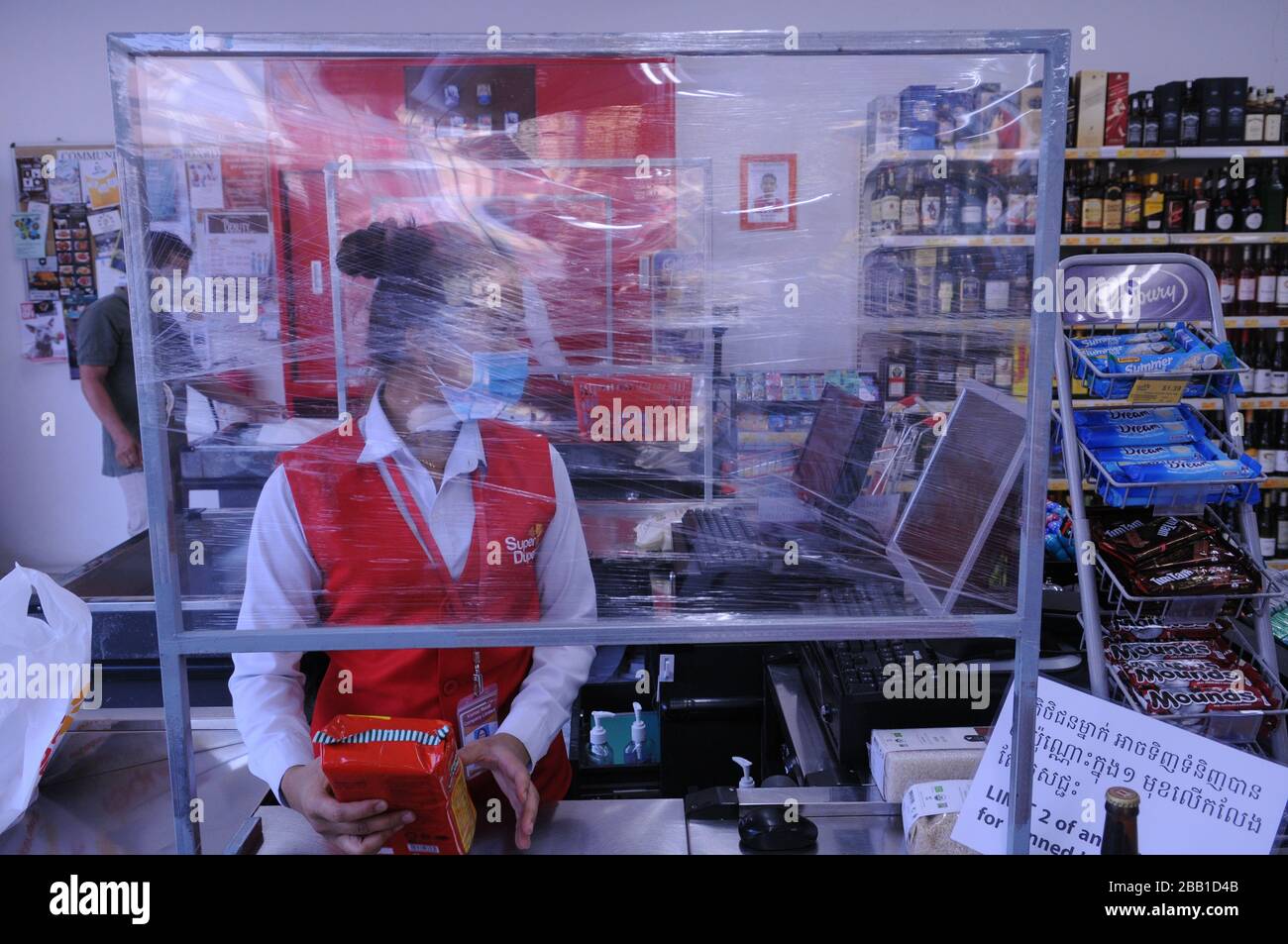 Un caissier de supermarché porte un masque de visage derrière un bouclier en plastique fait maison pendant la pandémie de coronavirus. Phnom Penh, Cambodge. © Kraig Lieb Banque D'Images