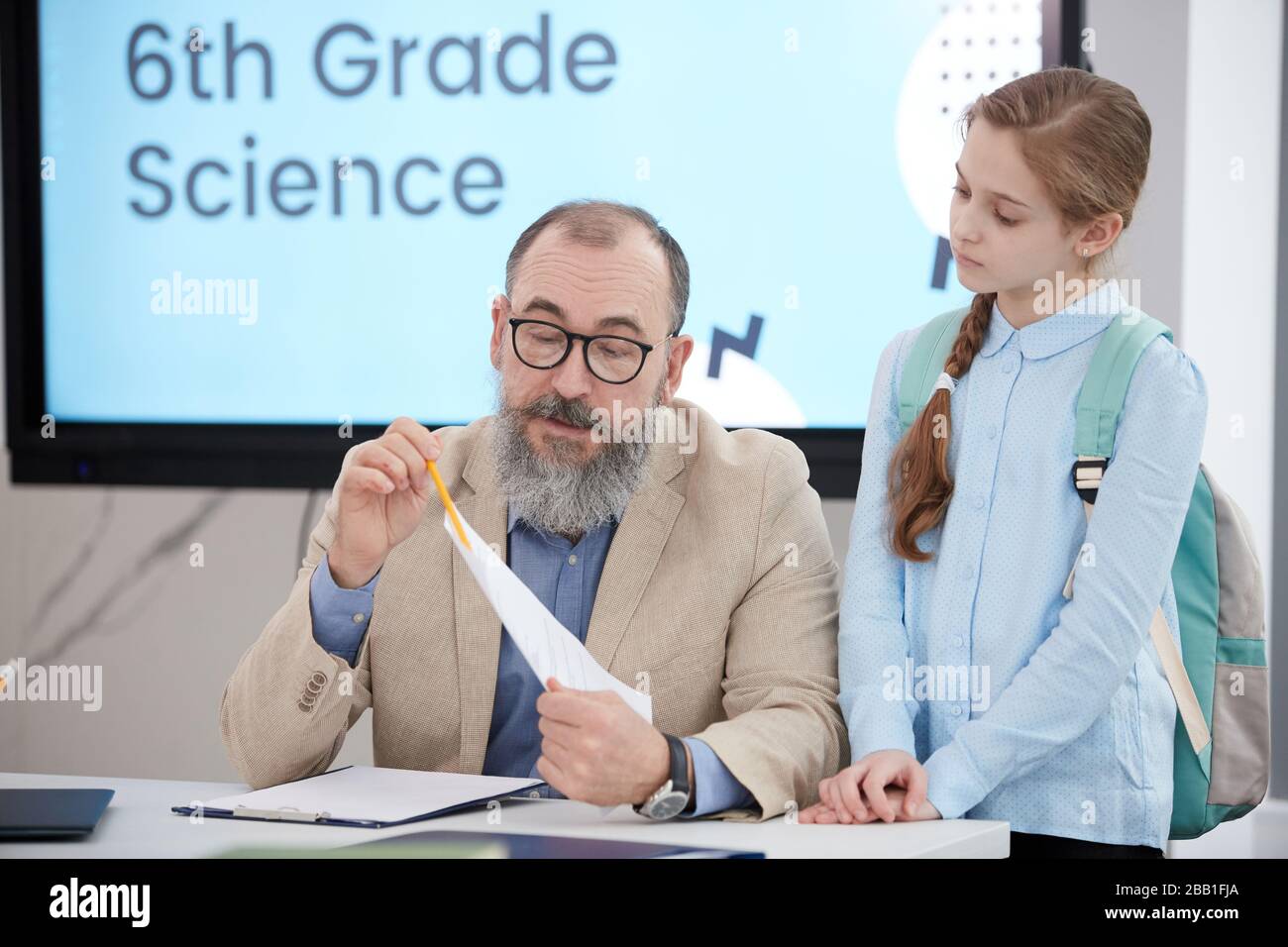 Portrait de l'enseignant senior barbu parlant à la mignonne écolière pendant le test de notation en classe, espace de copie Banque D'Images