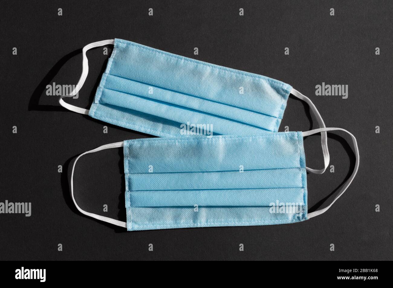 Deux masques médicaux jetables bleu clair sur fond noir foncé contre le virus covid-2019. Concept de soins de santé, quarantaine, arrêt du coronavirus Banque D'Images