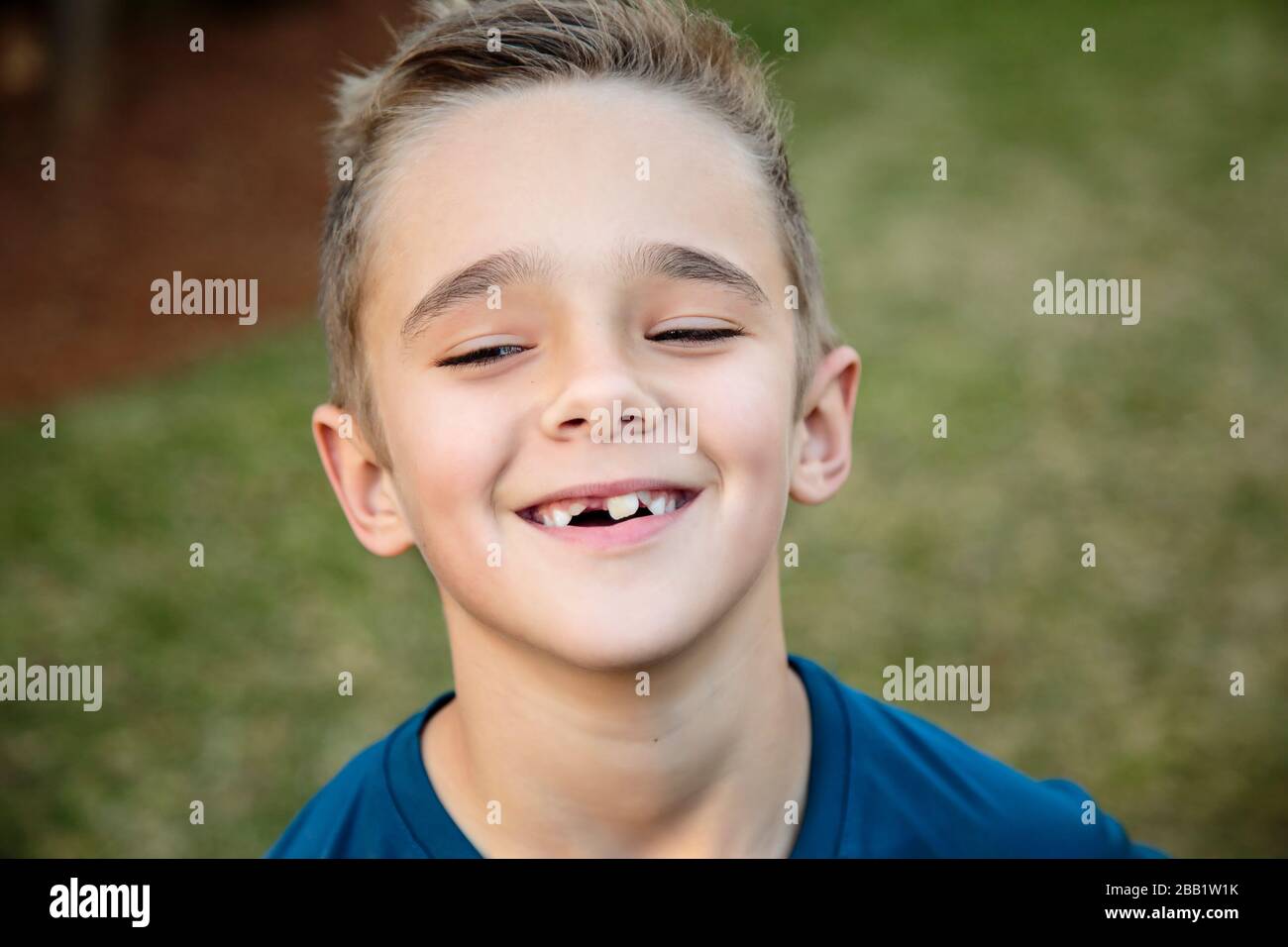 Gros plan d'un jeune garçon souriant avec sa tête inclinée un peu vers le haut, il a quelques dents manquantes Banque D'Images
