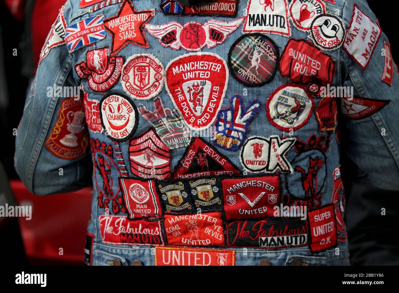 Un fan de Manchester United porte une veste en denim avec de nombreux patchs de club cousus sur le dos et les bras Banque D'Images