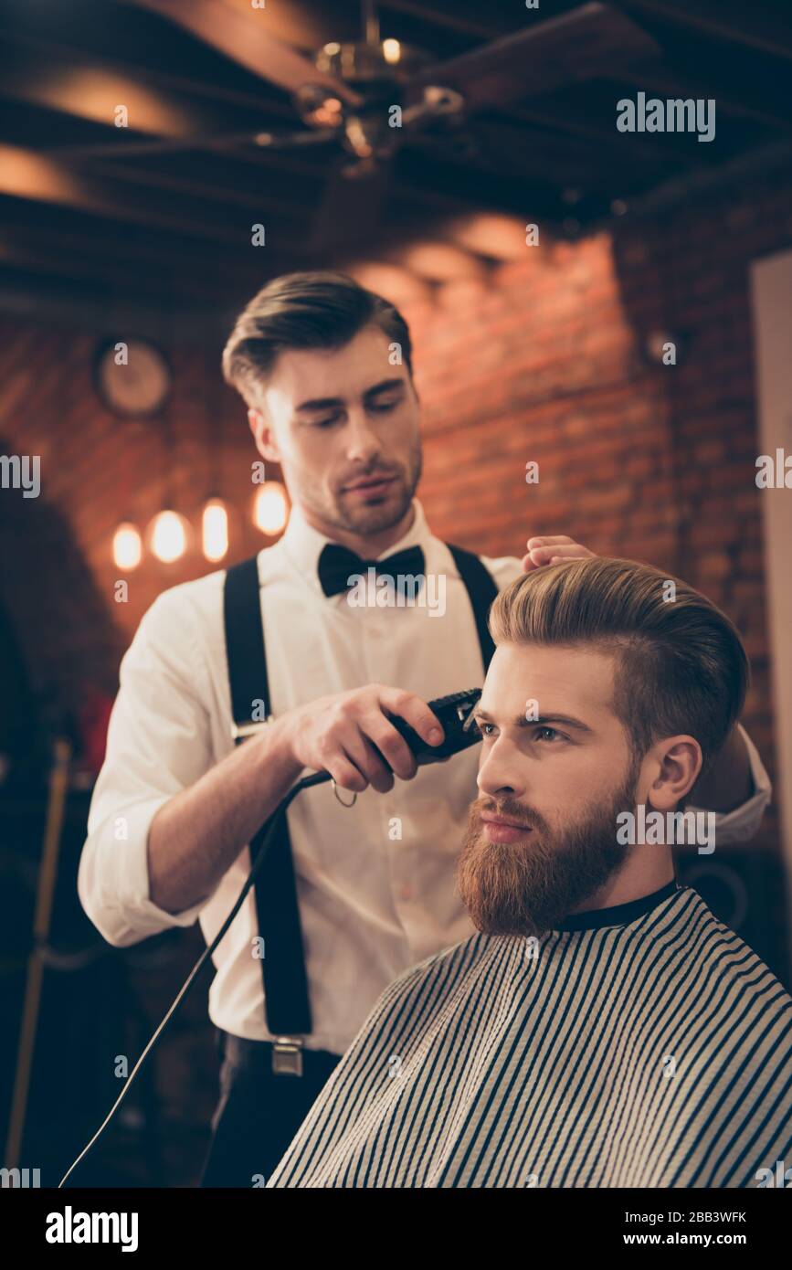 Coiffage de barbe pour un joli jeune gars au salon de coiffure. Le coiffeur est attrayant et porte une tenue classique, il est concentré et sérieux Banque D'Images