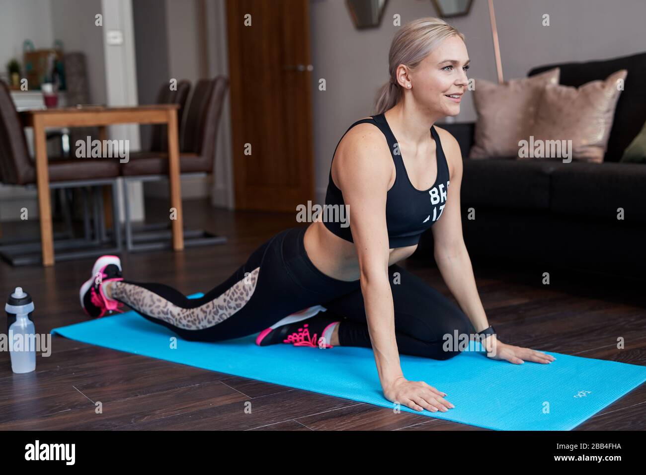 Une femme blond simple s'étire lorsqu'elle s'exerce à la maison sur un tapis dans le salon de son appartement Banque D'Images