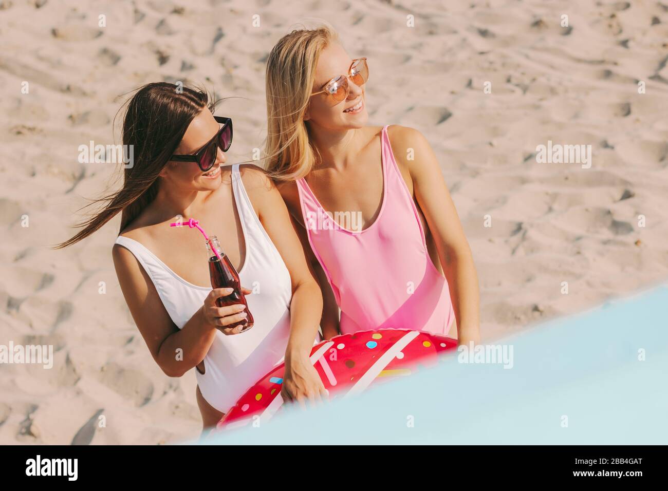 Portrait de deux jeunes femmes belles amis dans des maillots de bain et des lunettes de soleil élégants regardant loin et souriant tout en se posant à la plage ensoleillée. Attrayant che Banque D'Images
