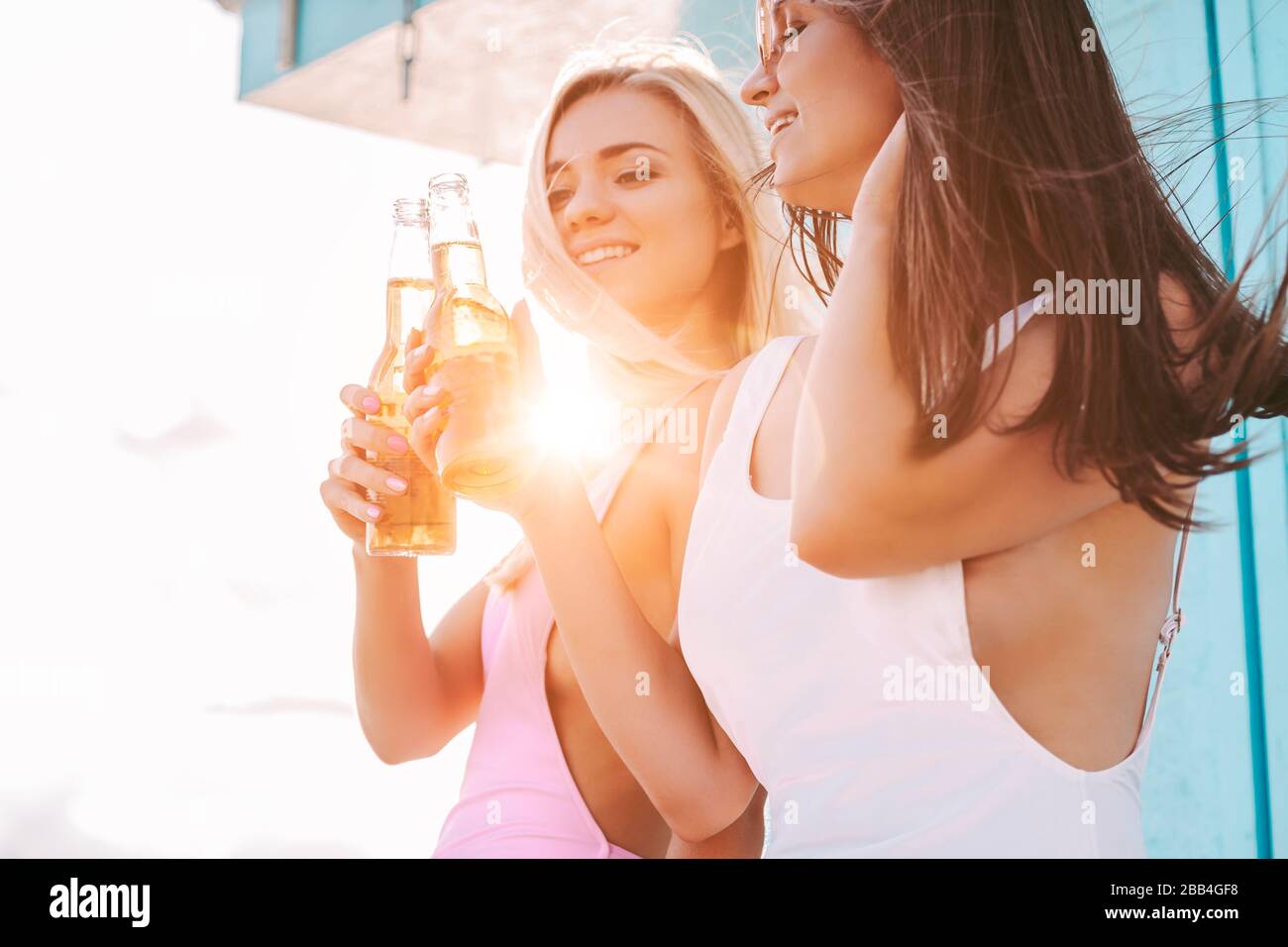 Portrait de deux belles filles acclamer et se posant avec des bouteilles de bière au bord de la mer. Jeunes femmes attrayantes amis boire de la bière froide et s'amuser Banque D'Images