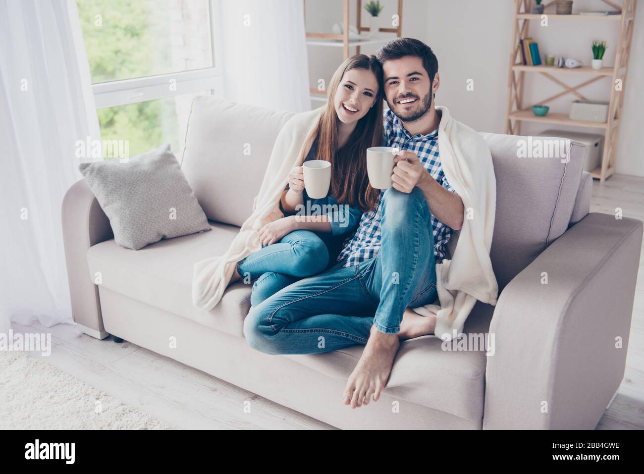 Vrai amour. Un couple romantique et gai est assis sur un canapé sous un plat confortable et souriant. Ils boivent du thé, portent des vêtements décontractés, pieds nus Banque D'Images