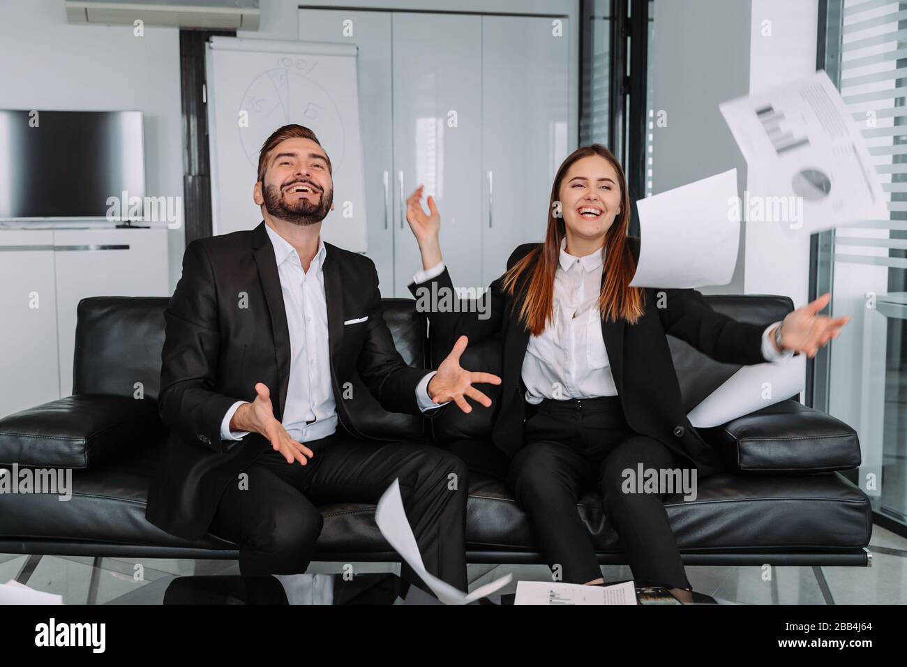 Au bureau moderne, deux hommes d'affaires et femmes d'affaires sont avides feuilles de papier dans l'air après avoir fini de travailler et réussi sur leur but Banque D'Images