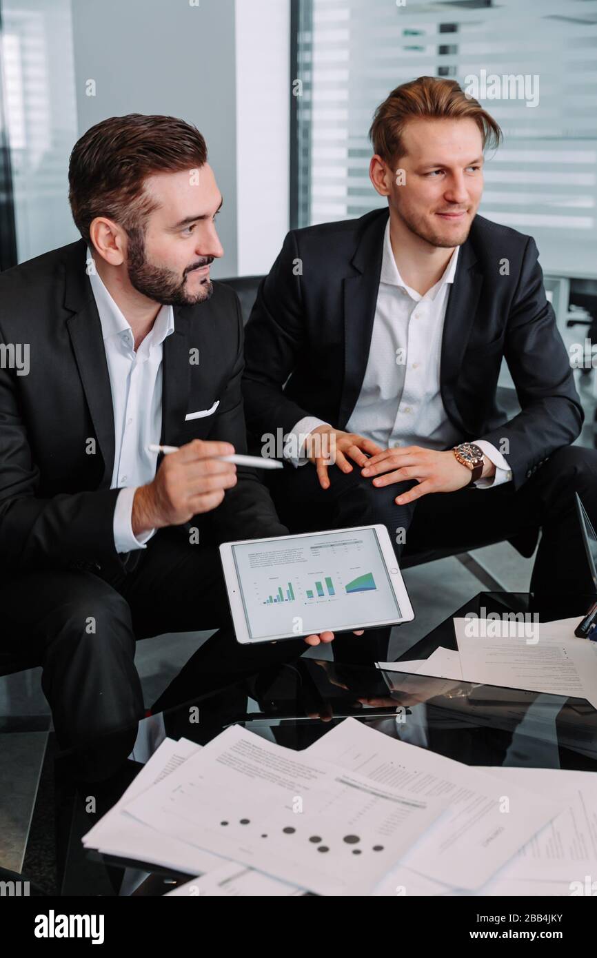 deux jeunes investisseurs commerciaux qui parlent et lisent des informations sur les statistiques financières dans la tablette mobile ensemble assis au bureau, financ Banque D'Images