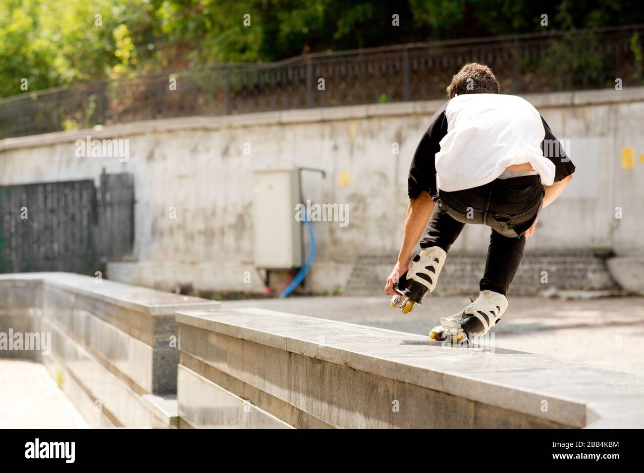 Vue arrière du jeune patineur professionnel faisant des cascades dehors. Vue urbaine moderne. Patinage sur une jambe. Sortie de lumière du jour. Banque D'Images