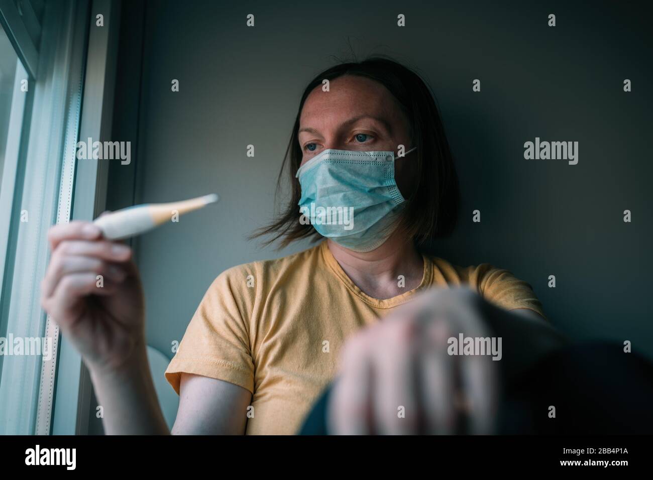 Femme en auto-isolation mesurant la température corporelle thermomètre numérique électronique. Femme avec masque respiratoire protecteur du visage, fcu sélectif Banque D'Images