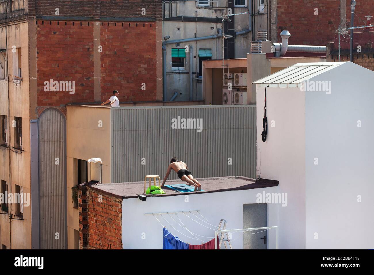 Deux hommes s'exercent sur leurs terrasses respectives sur le toit pendant la deuxième semaine de maintien à Barcelone, en Espagne. Banque D'Images