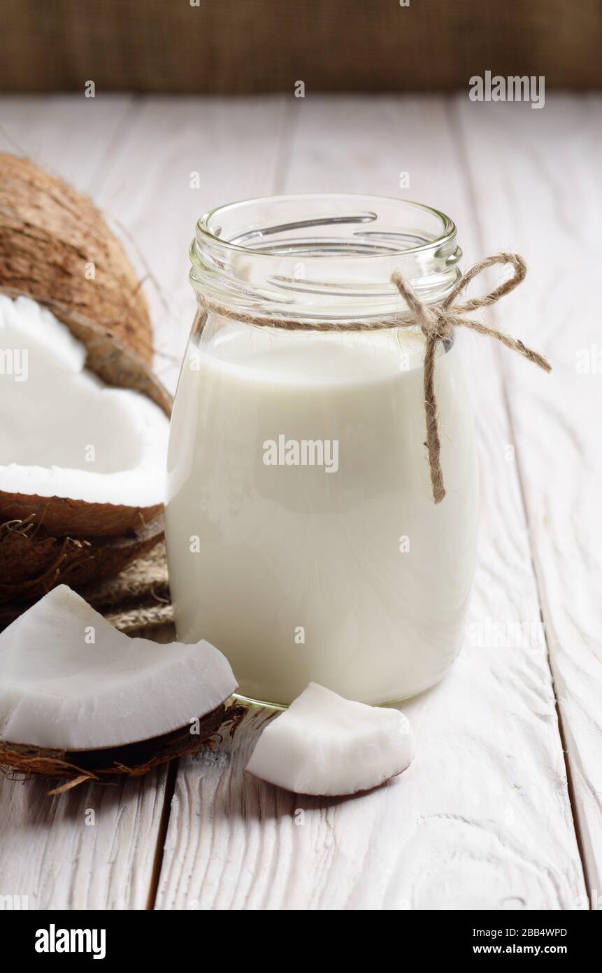 Bouteille de verre avec lait ou yaourt sur table de cuisine en bois blanc avec noix de coco de côté Banque D'Images