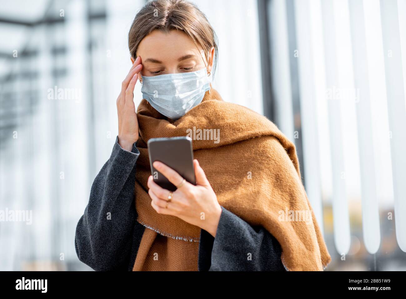 Une jeune femme déprimée en masque de visage s'inquiétait de lire de mauvaises nouvelles sur un smartphone à un arrêt des transports publics pendant une épidémie. Concept de panique et mauvaise influence des nouvelles Banque D'Images