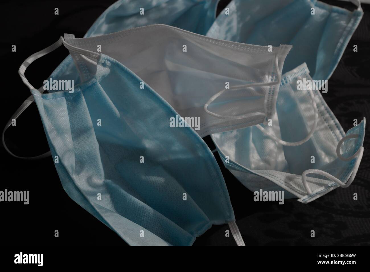 Cinq masques médicaux jetables à usage bleu clair sur fond noir foncé avec ornements d'ombres contre le virus covid-2019. Concept de soins de santé Banque D'Images