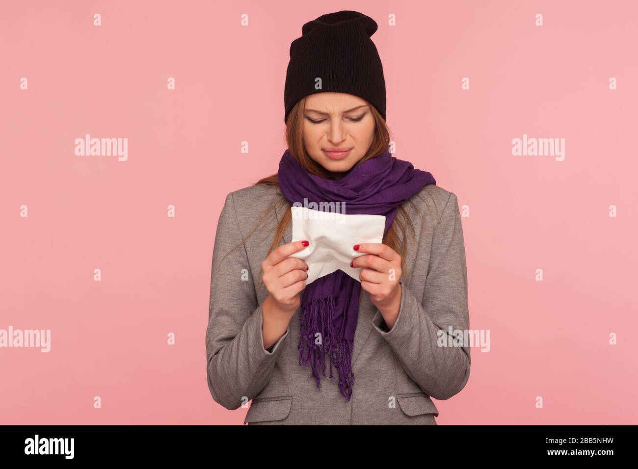 Portrait d'une femme malade de la grippe déprimée dans un chapeau chaud et un foulard tenant des tissus, souffrant de nez liquide, éternué et haute température, symptômes de la grippe. indo Banque D'Images