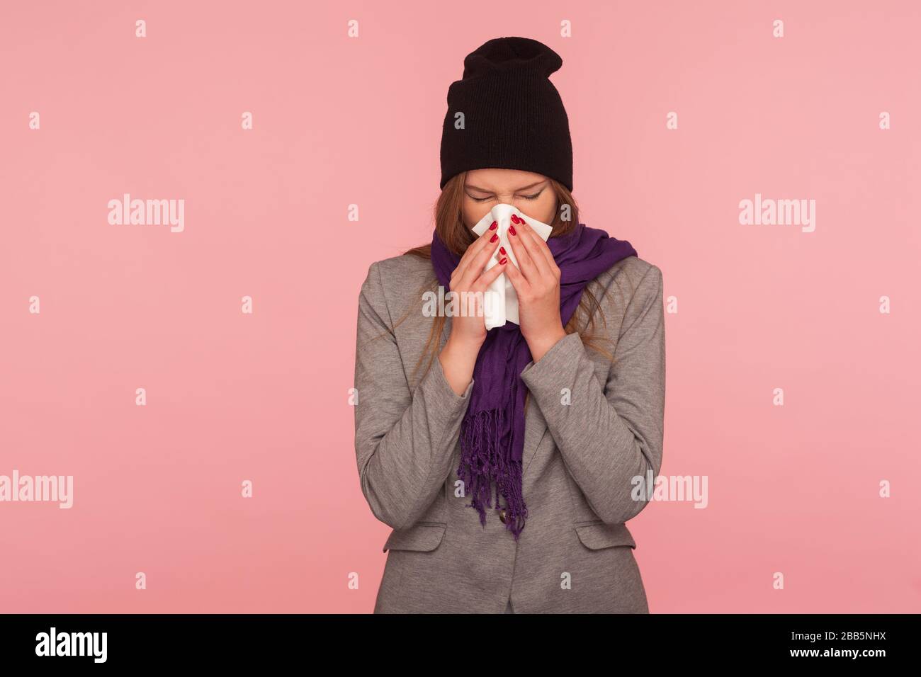 Grippe saisonnière. Portrait d'une femme malade de la grippe dans un chapeau chaud et un foulard soufflant le nez dans les tissus, éternuant souffrant de symptômes d'allergie, se sentant malsain. i Banque D'Images