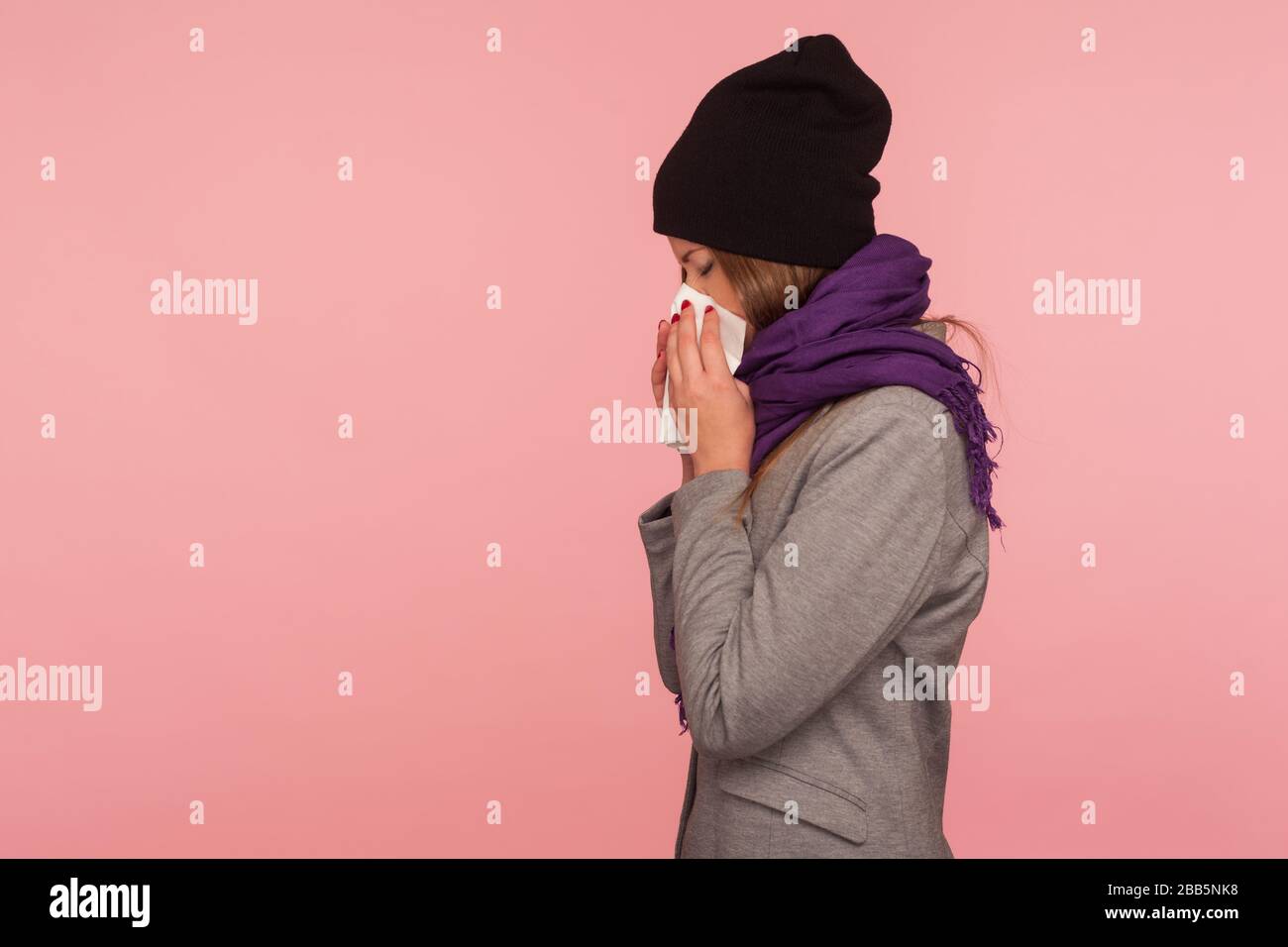 Grippe saisonnière. Vue latérale d'une femme malade de la grippe dans un chapeau chaud et un foulard soufflant le nez dans les tissus, éternuant souffrant de symptômes d'allergie, se sentant malsain. Banque D'Images