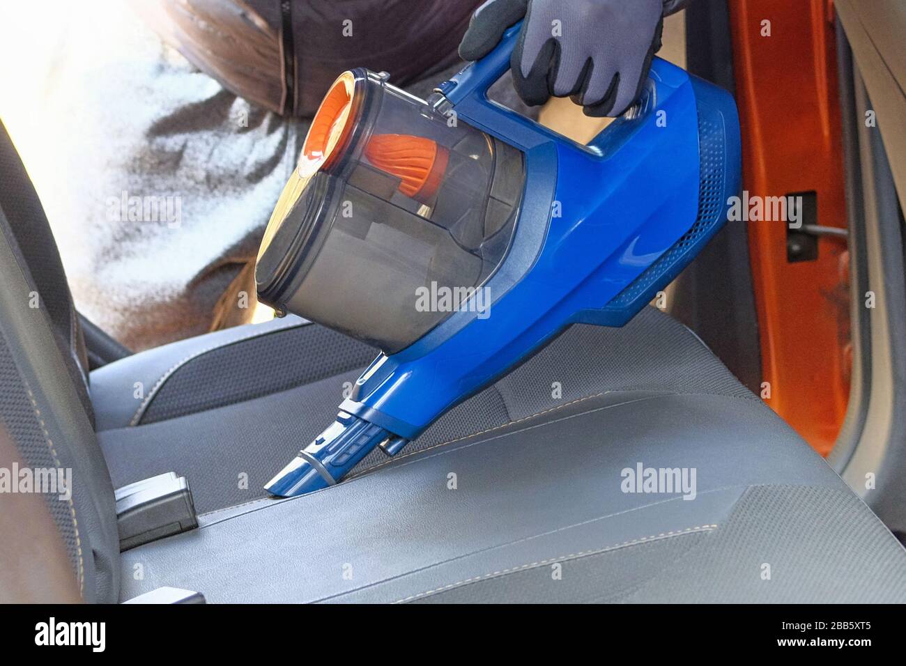 Aspirateur entre les mains du conducteur. Nettoyage de l'intérieur de l'automobile avec aspirateur bleu, fermeture. Les sièges en textile de voiture sont régulièrement nettoyés. Banque D'Images