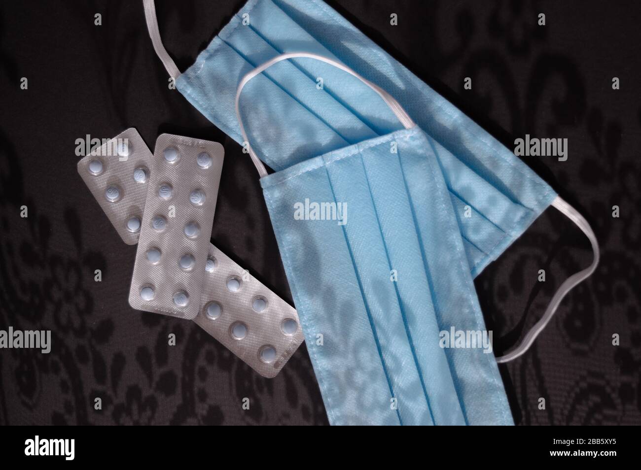 Comprimés et deux masques médicaux jetables bleu clair sur le fond sombre avec des ornements d'ombres contre le virus covid-2019. Concept de soins de santé Banque D'Images