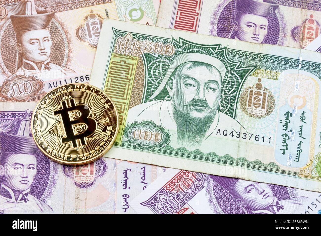 Gros plan sur une pièce de monnaie en Bitcoin doré au-dessus d'une pile de billets en Tögrög mongol. Banque D'Images