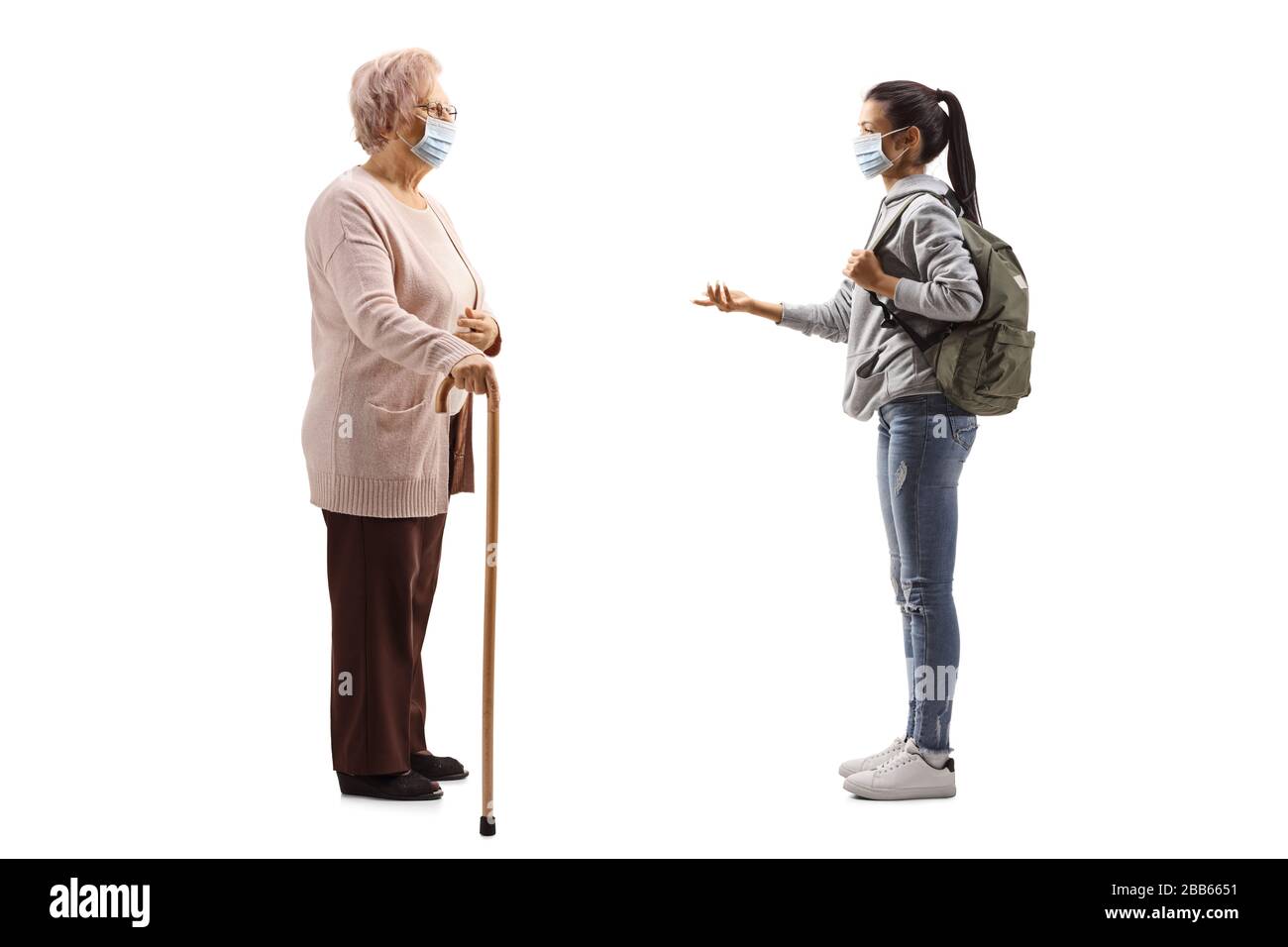 Photo de profil pleine longueur d'une étudiante féminine avec masque médical de protection ayant une conversation avec une femme âgée isolée sur fond blanc Banque D'Images