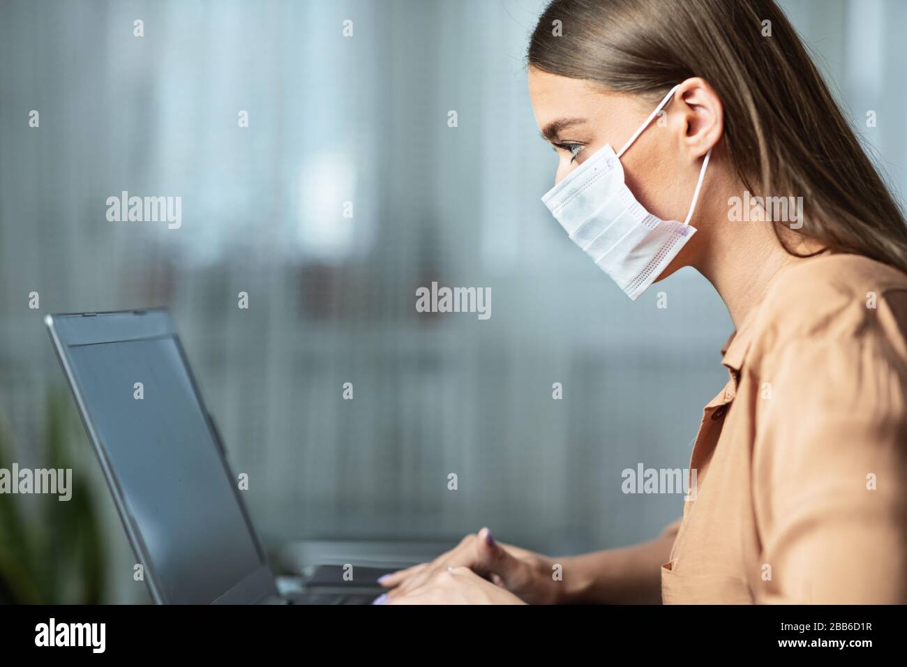 Femme portant un masque facial et travaillant sur un ordinateur portable Banque D'Images