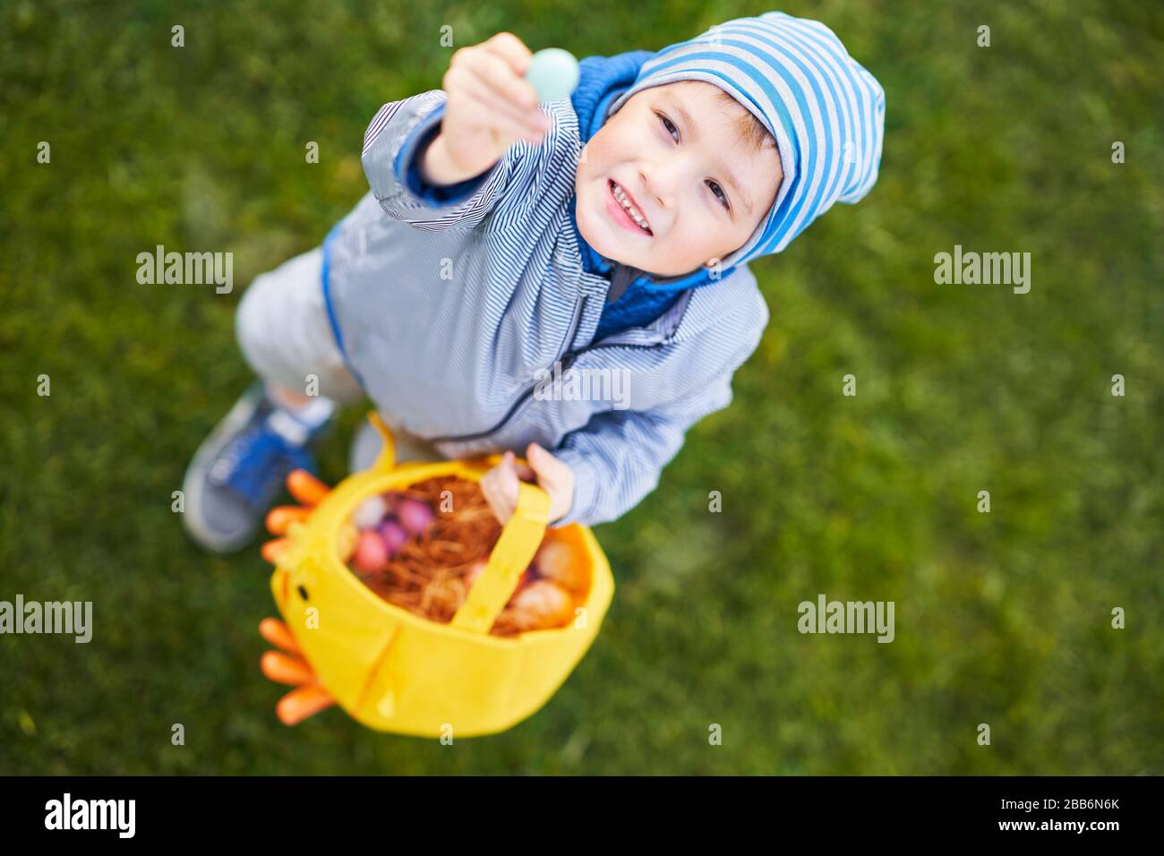 Petit garçon portant un masque de protection pour la chasse à l'oeuf de Pâques dans le jardin de printemps. Banque D'Images