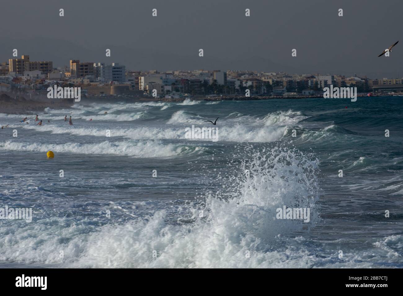 Les gens se baignent dans une mer Méditerranée pluvieuse dans un après-midi d'été venteux avec la ville andalouse de Garrucha en arrière-plan Banque D'Images