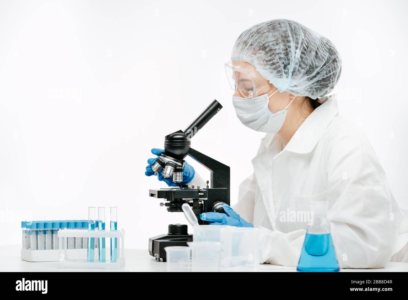 l'employé dans le masque de protection et l'uniforme à l'aide du microscope effectue un test de coronavirus Banque D'Images