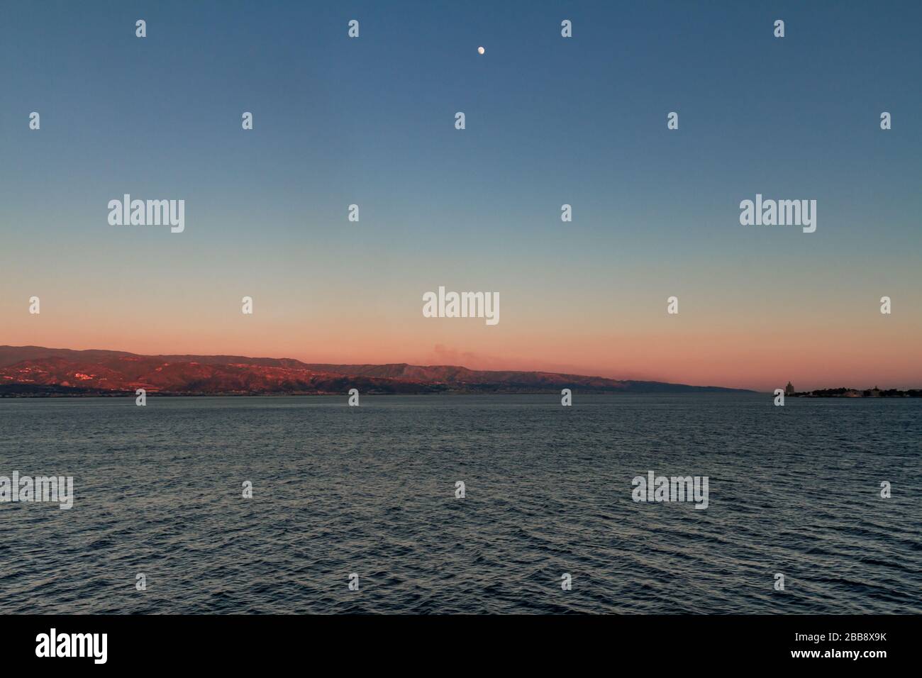 Vue sur le Stretto di Messina du ferry qui le traverse, avec une lune illuminante et un phare à droite Banque D'Images