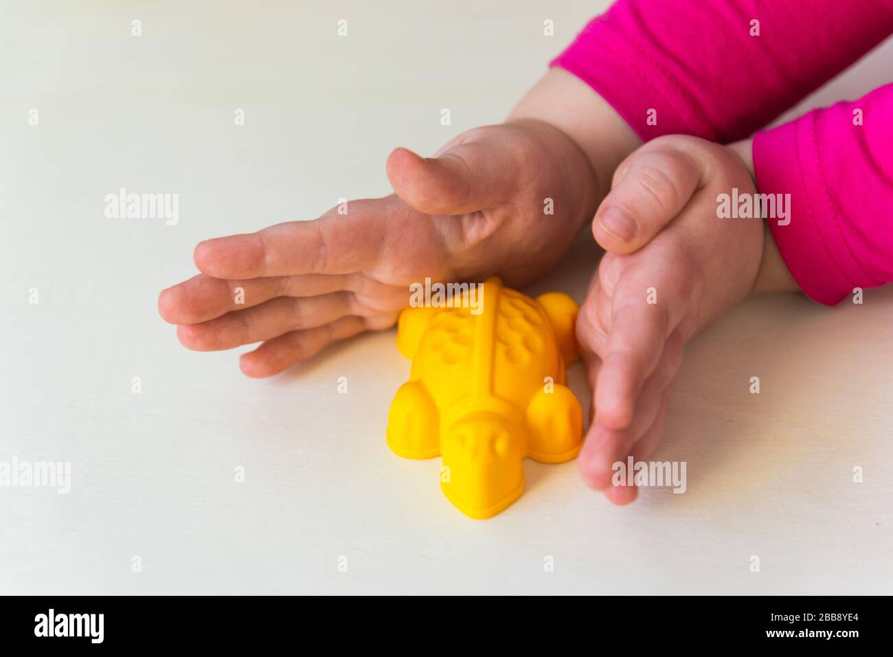 Mains de l'enfant tenant les petits jouets sur le fond de bois. Tortue en plastique jaune. Banque D'Images