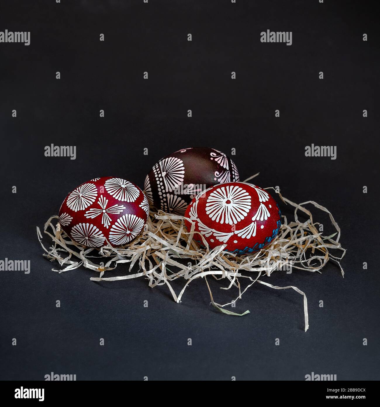 Trois œufs traditionnels lituaniens peints en rouge, noir, blanc et bleu avec de la cire, appelés marguciai, dans le nid de paille sur fond noir. Copier le collage Banque D'Images