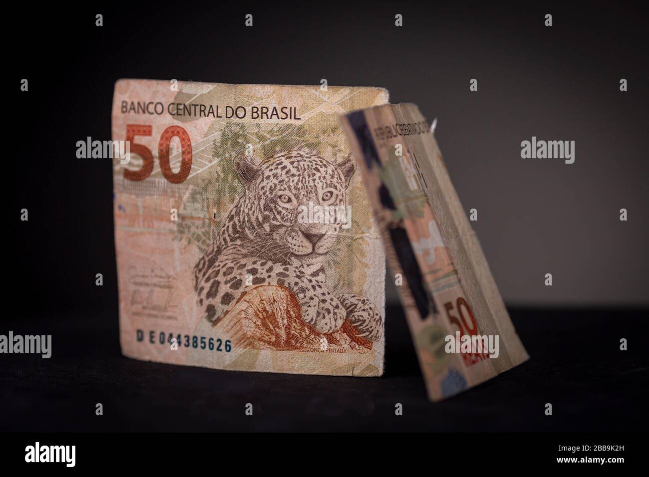 Gros plan sur deux moitiés d'un billet de banque Real brésilien debout. Le studio à touches faibles offre encore une vie avec une surface noire et un arrière-plan gris foncé Banque D'Images