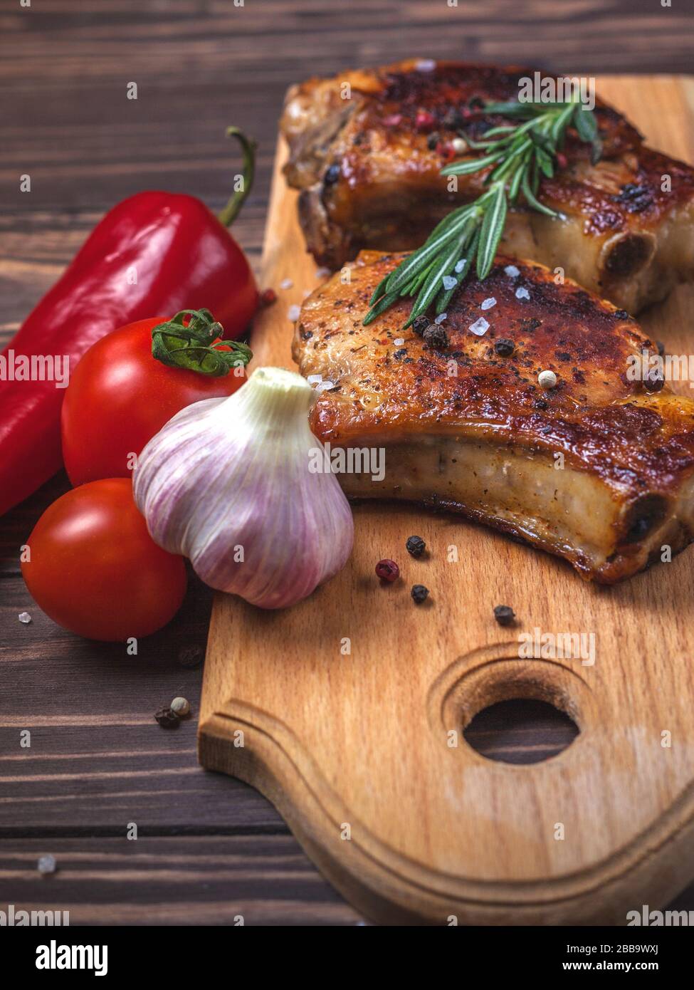 Steaks et légumes de porc grillés sur une table en bois rustique. Viande grillée sur l'os avec épices, ail, poivrons, tomates et romarin. Menu du restaurant Banque D'Images