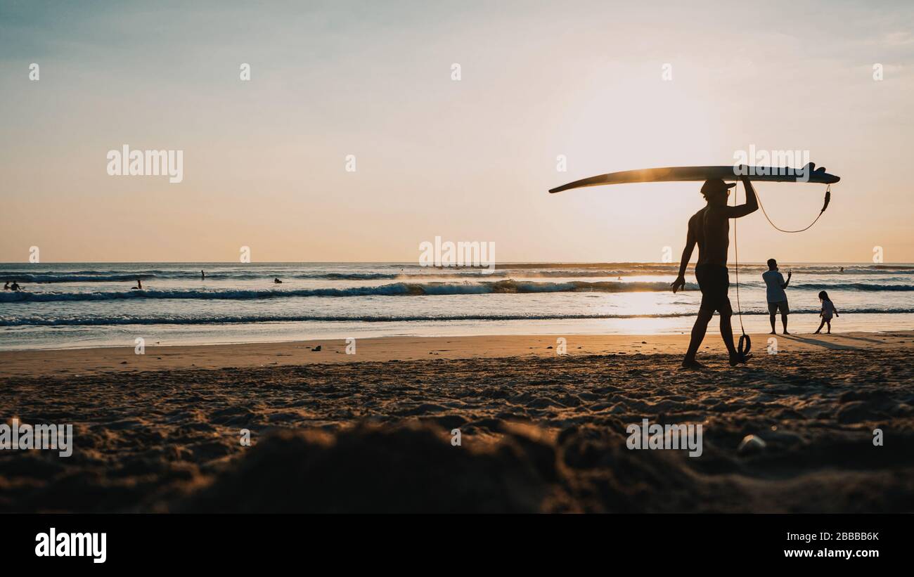 Les silhouettes des surfeurs marchent sur la plage au coucher du soleil Banque D'Images