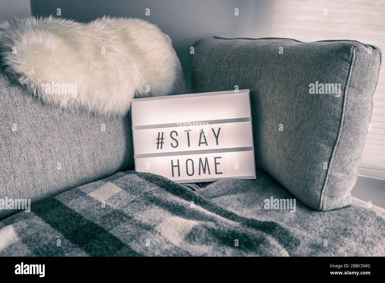Coronavirus maison visionneuse signe avec hashtag message Hashtag STAYHOME brillant sur le canapé maison avec confortable fourrure de laine d'agneau, couverture. Texte COVID-19 pour promouvoir l'auto-isolation rester à la maison. Banque D'Images