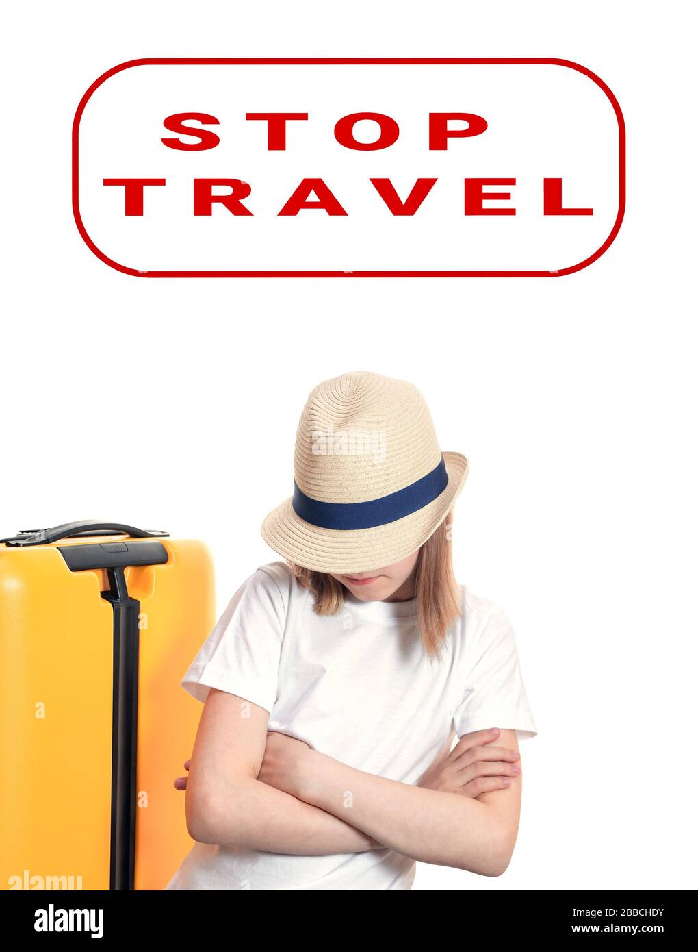Une jeune femme de tourisme avec chapeau sur le visage garde les mains croisées sur la poitrine près de la valise jaune sur les roues isolées sur blanc. Arrêtez la bannière de voyage sur sa tête. P Banque D'Images