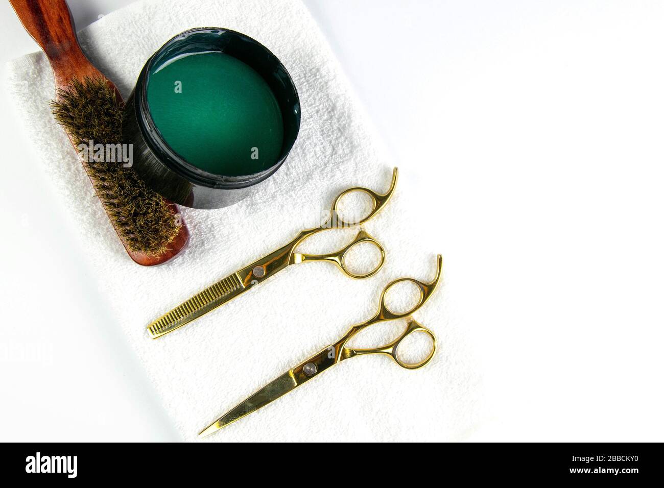 Gel pour cheveux, peigne et ciseaux pour le support de coupe sur une serviette blanche qui se tient sur un fond blanc Banque D'Images