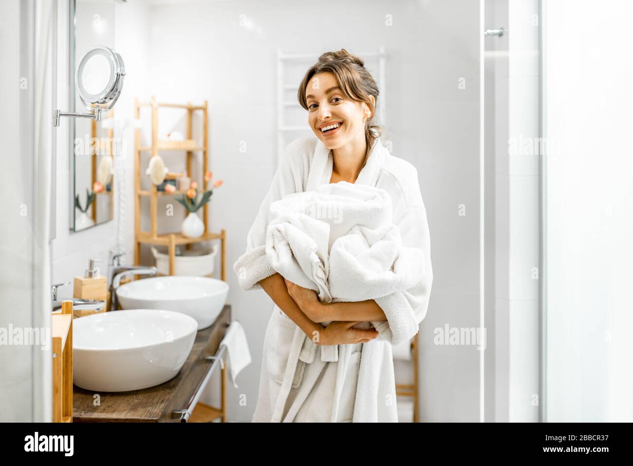 Jeune femme en peignoir faisant des travaux ménagers, debout avec des serviettes dans la salle de bains Banque D'Images