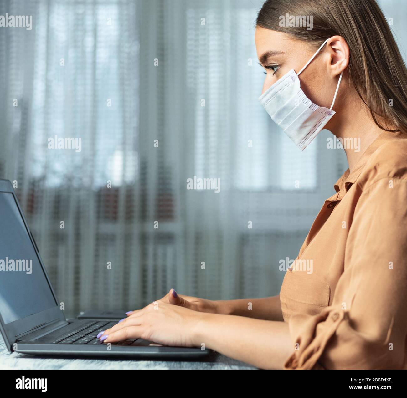 Femme portant un masque facial et travaillant sur un ordinateur portable, gros plan Banque D'Images