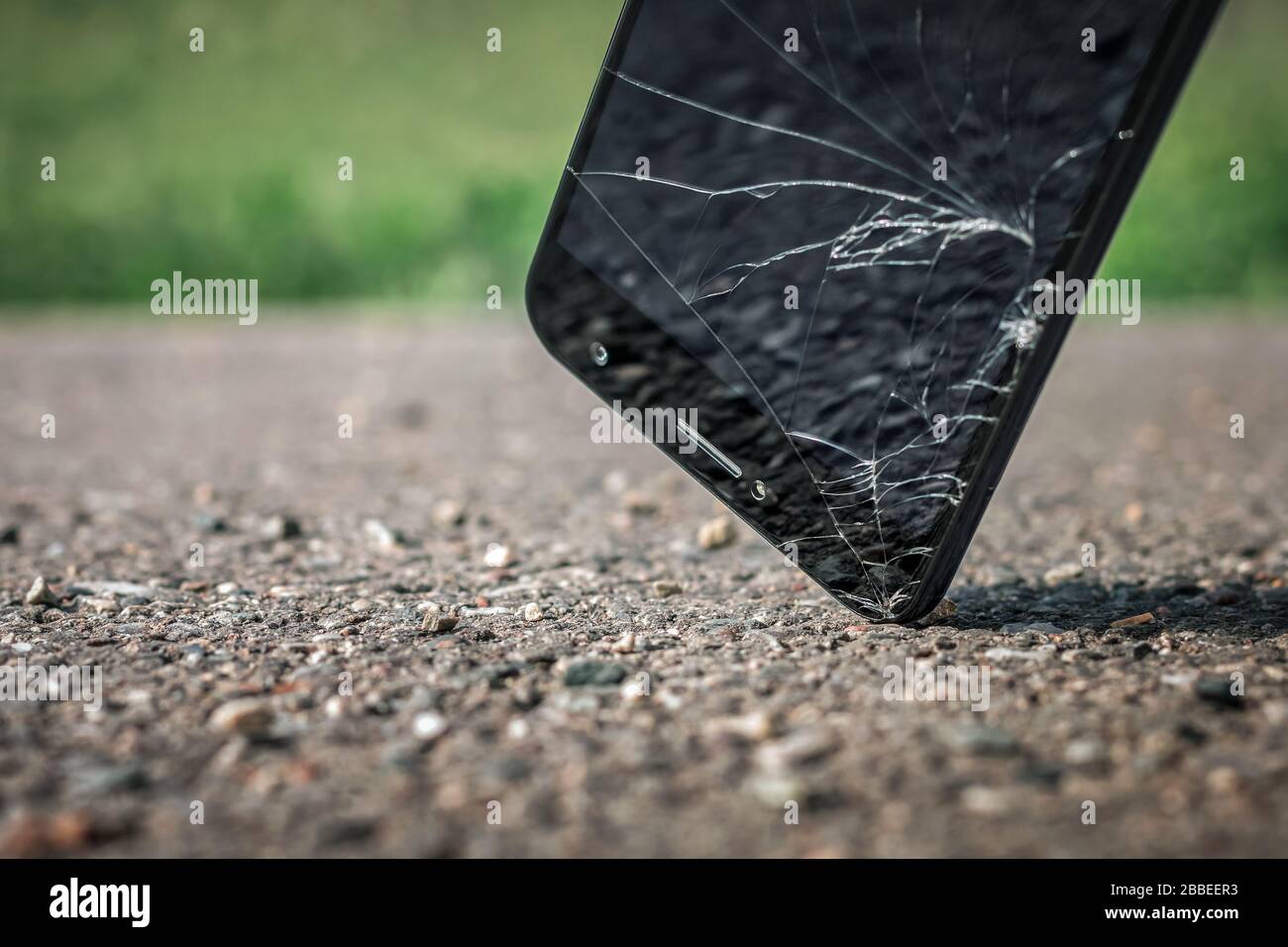Gros plan d'un smartphone noir moderne qui tombe sur de l'asphalte dur, frappé par le coin de l'écran et cassé. L'affichage est craquelé. Banque D'Images