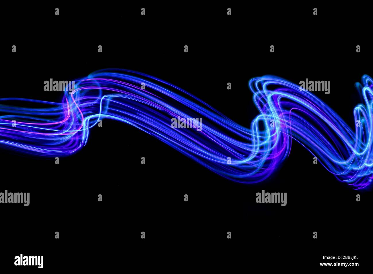 Photographie de longue exposition de couleur néon vive dans un tourbillon abstrait, lignes parallèles modèle contre un fond noir. Photographie de peinture légère. Banque D'Images