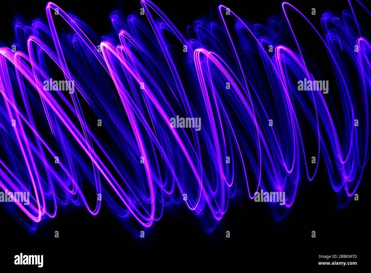 Photographie de longue exposition de couleur néon vive dans un tourbillon abstrait, lignes parallèles modèle contre un fond noir. Photographie de peinture légère. Banque D'Images
