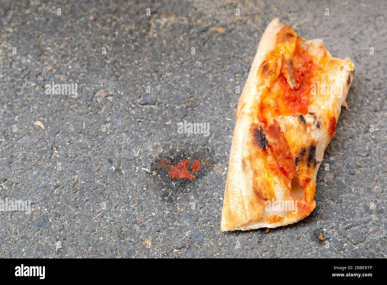 Petit morceau de croûte de pizza jetée, il est couché sur de l'asphalte. Banque D'Images