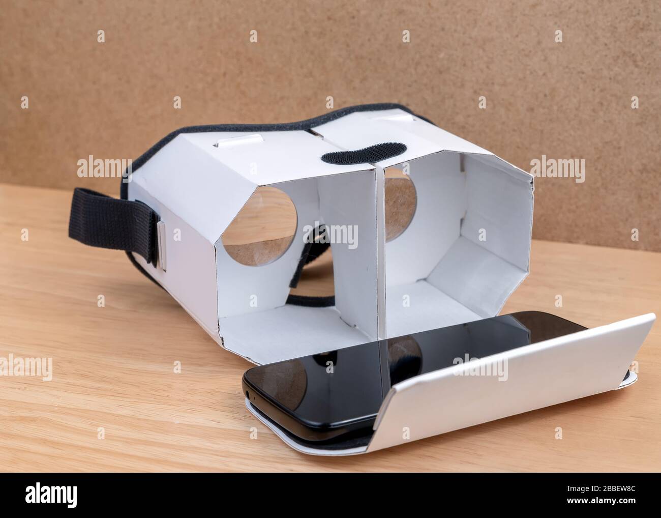 Un casque en carton pour la réalité virtuelle. Vue de face, il est ouvert un téléphone mobile sur lui. Lentilles visibles à l'intérieur. Il repose sur une table en bois à côté d'un cor Banque D'Images