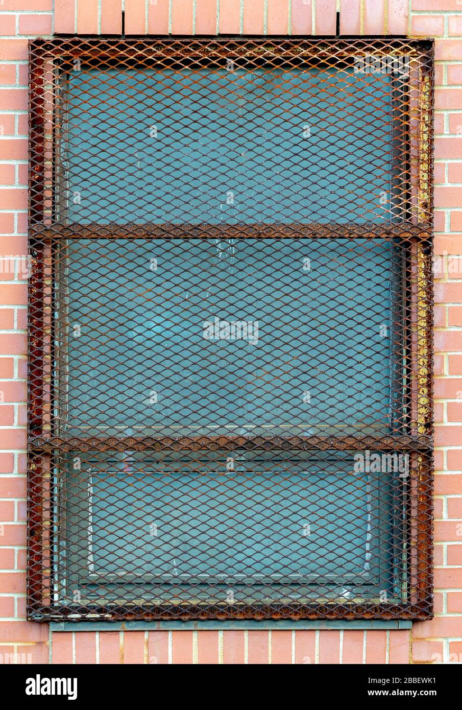 Un écran en métal lourd protégeant la fenêtre dans un bâtiment en brique. L'écran est en forme de losange et rouillé. Banque D'Images