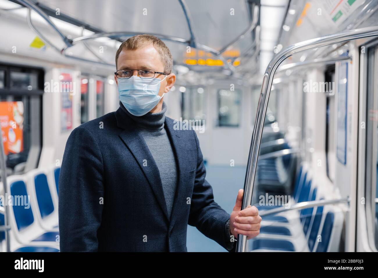 Les hommes de banlieue poses dans un chariot de métro vide, portent un masque médical pour empêcher les coronavirus infectés à la station de métro publique, regarde quelque part, pense abou Banque D'Images