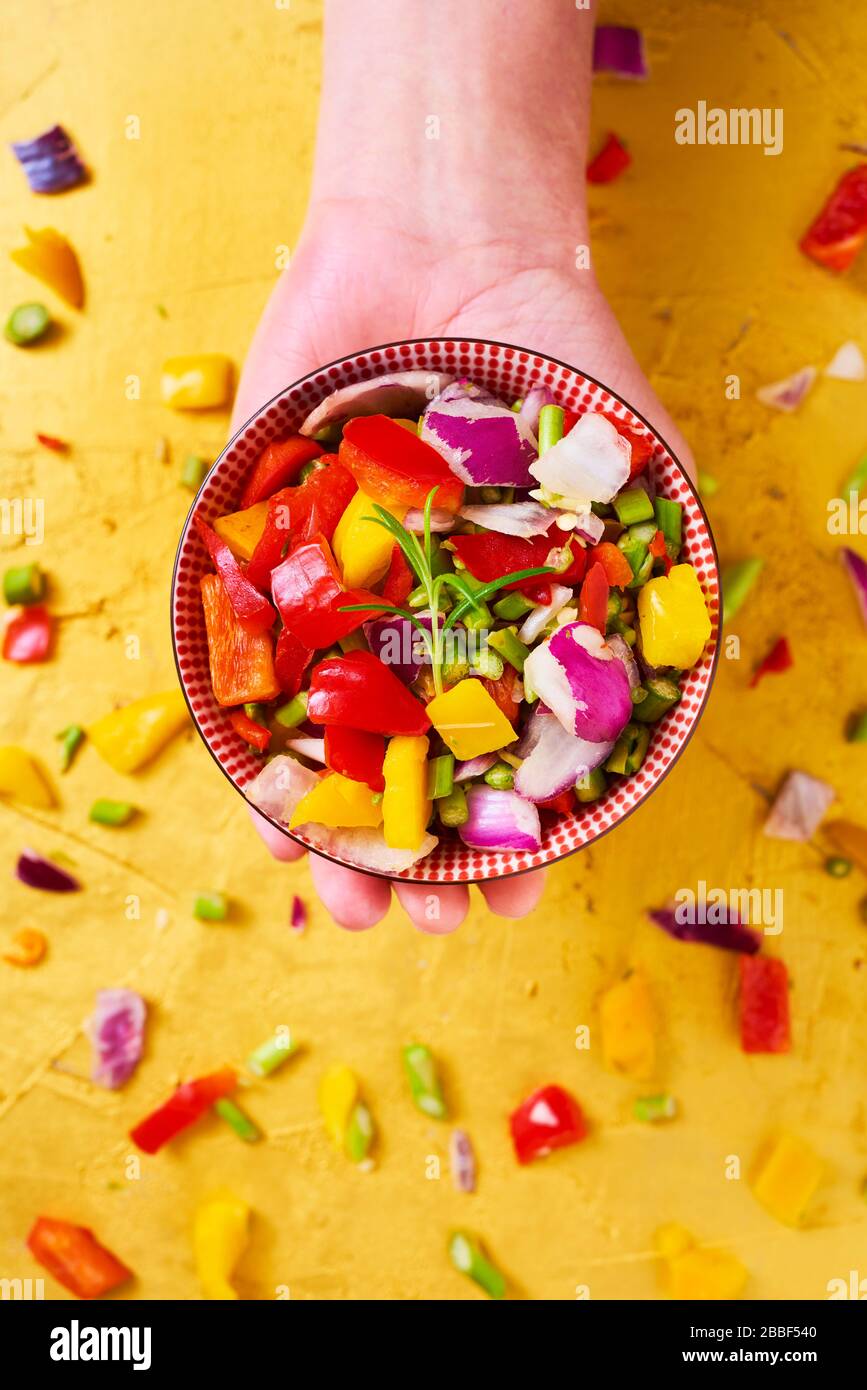 vue en grand angle d'un bol avec un mélange de différents légumes crus hachés, tels que l'asperge, l'oignon ou le poivron jaune et rouge, à la main d'une ma Banque D'Images